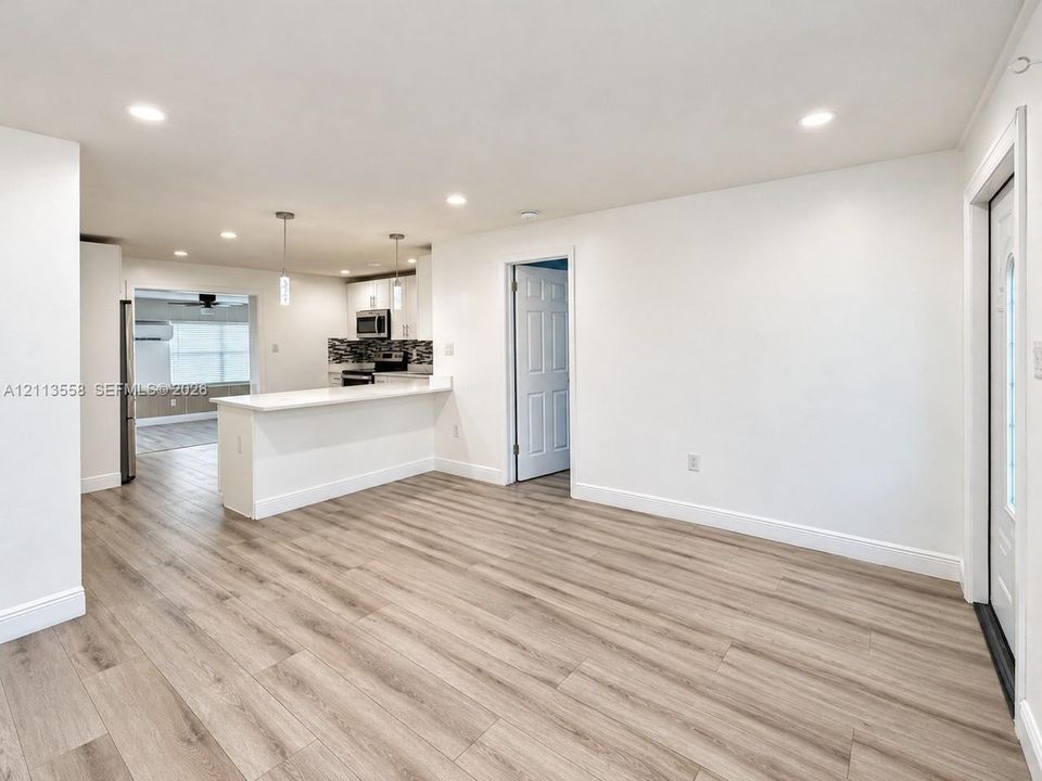 Open-concept interior featuring wood-finish flooring, recessed lighting, a kitchen breakfast bar, pendant lighting, and a multi-panel interior door