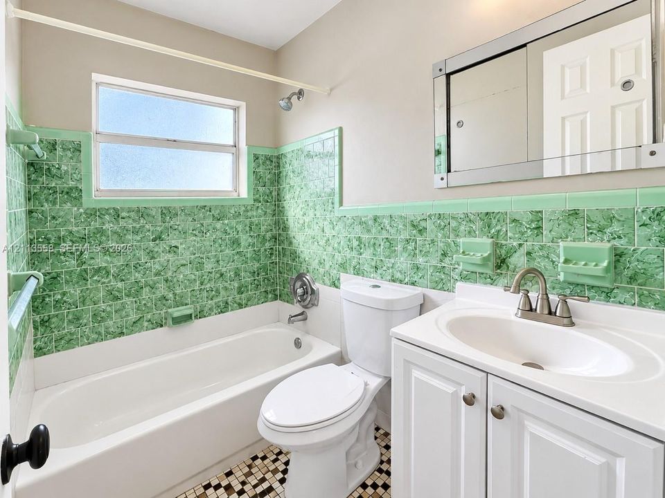 Bathroom featuring green mosaic tile wall surrounds, a white pedestal-style vanity with an integrated sink, a rectangular mirrored medicine cabinet, a standard-size soaking tub, and a checkered floor pattern