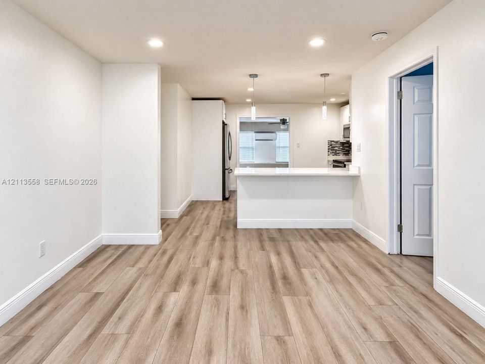 Open-concept interior featuring wood-finish flooring, recessed lighting, and a breakfast bar with quartz countertop