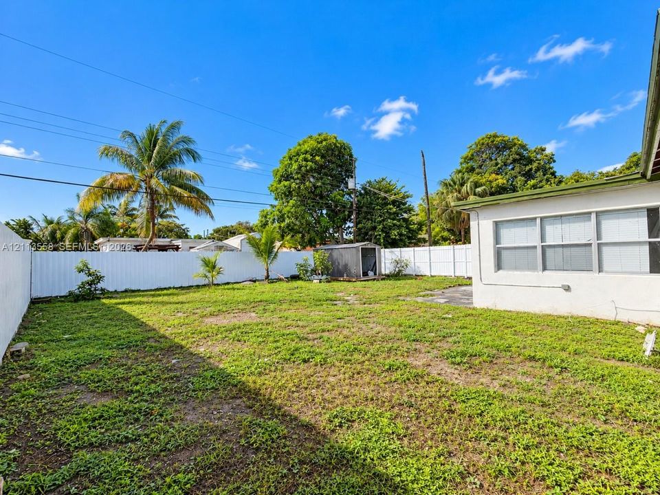 Backyard featuring a white vinyl privacy fence, detached storage structure, and mature palm trees