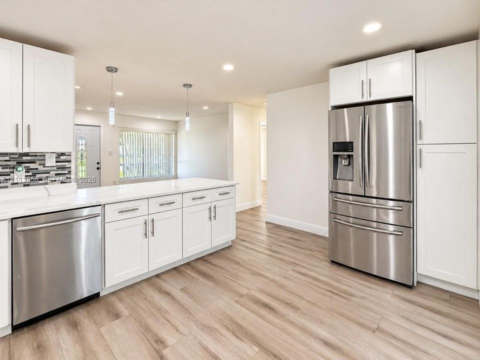 Kitchen featuring white shaker-style cabinetry, stainless steel appliances, quartz countertops, a multi-tonal mosaic tile backsplash, and wood-finish flooring