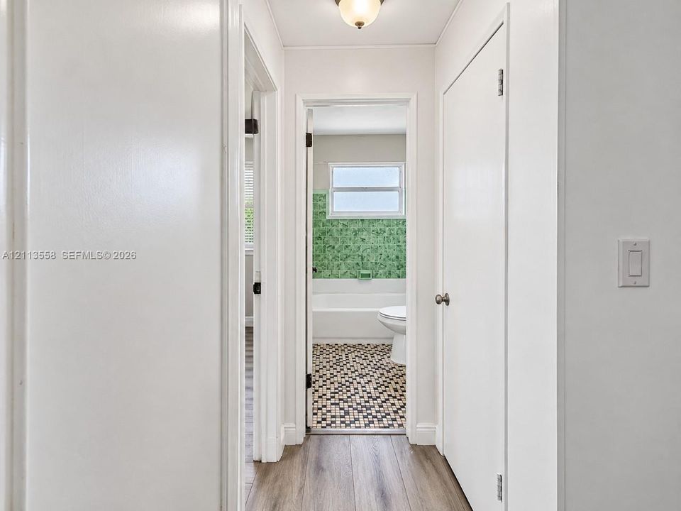 Interior hallway featuring wood-finish flooring, white flush-panel doors, and a ceiling-mounted light fixture