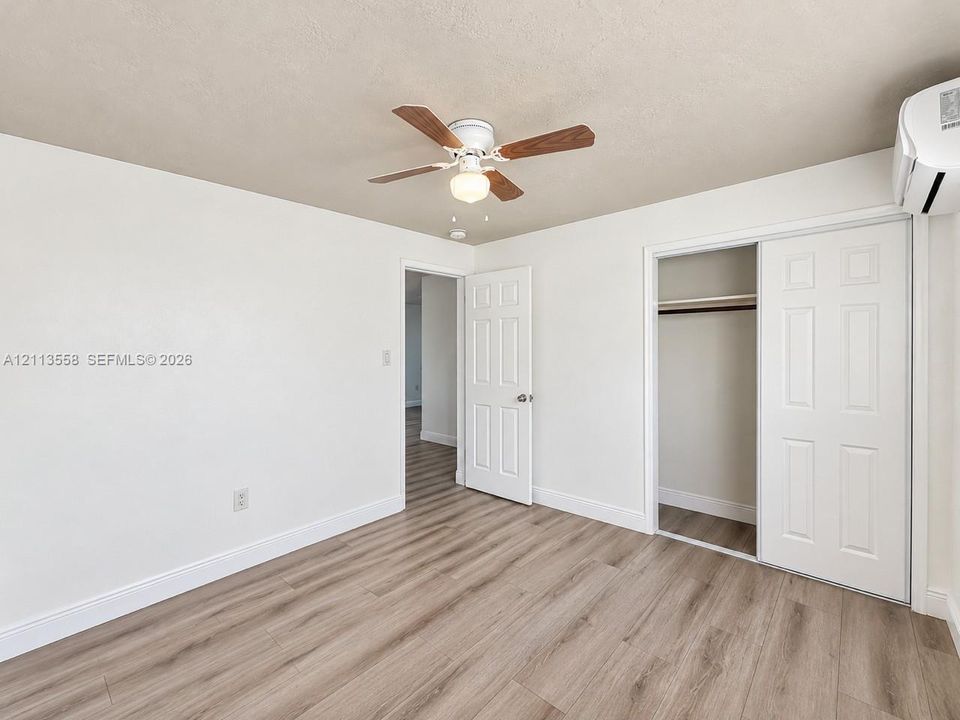 Room featuring wood-finish flooring, a wall-mounted climate control unit, a ceiling fan with integrated lighting, and a closet with sliding panel doors