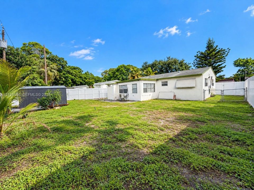 Expansive backyard featuring a white privacy fence, mature perimeter trees, and a detached metal storage structure