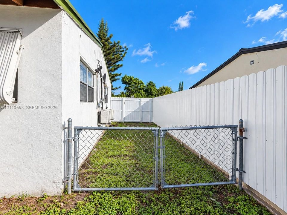 Exterior side yard featuring stucco siding, white vinyl privacy fencing, and a metal chain-link gate