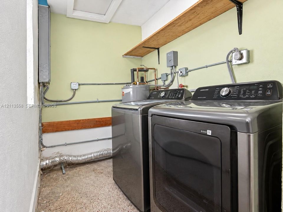 Laundry area featuring wall-mounted wooden shelving, concrete flooring, and exposed electrical and utility conduits
