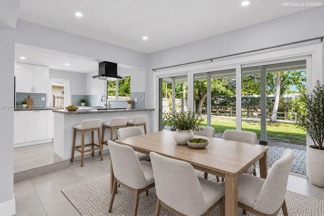 Kitchen featuring a peninsula with countertop seating, tiled backsplash, recessed lighting, and sliding glass doors leading to a paved patio