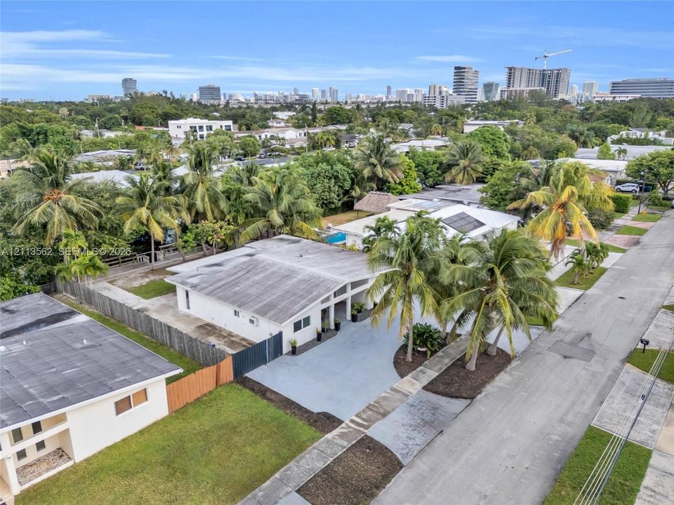 Single-story residence featuring a flat roofline, paved driveway, integrated solar panels, and mature palm landscaping