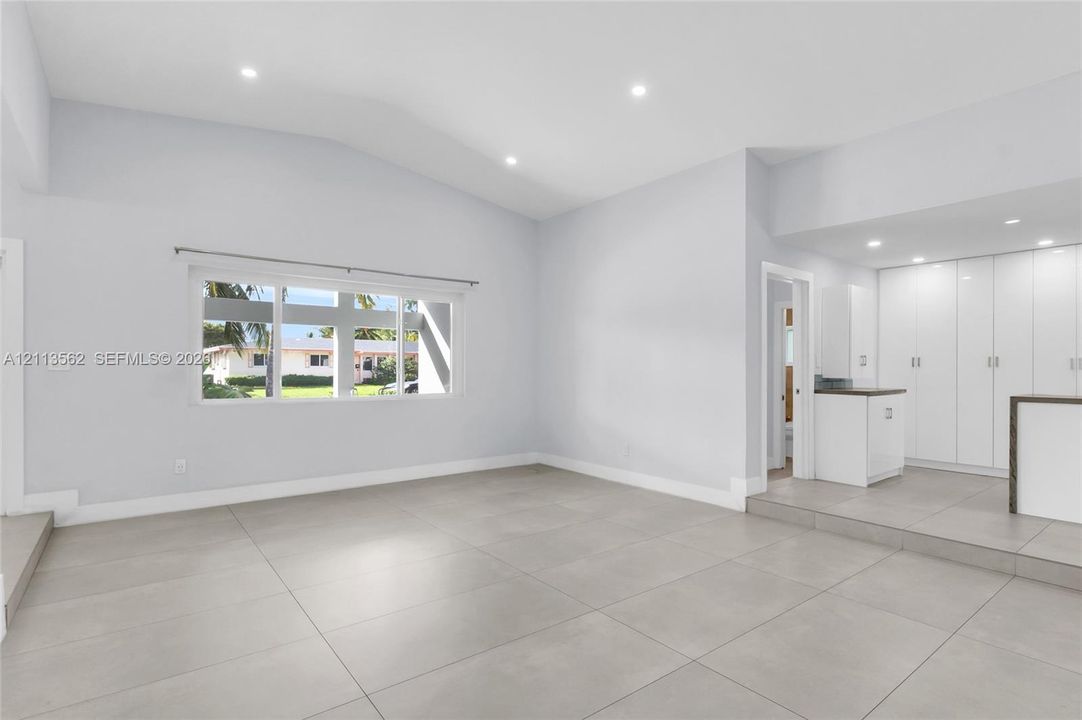 Open-concept space featuring vaulted ceilings, large-format tile flooring, recessed lighting, and built-in white cabinetry with a dedicated countertop surface