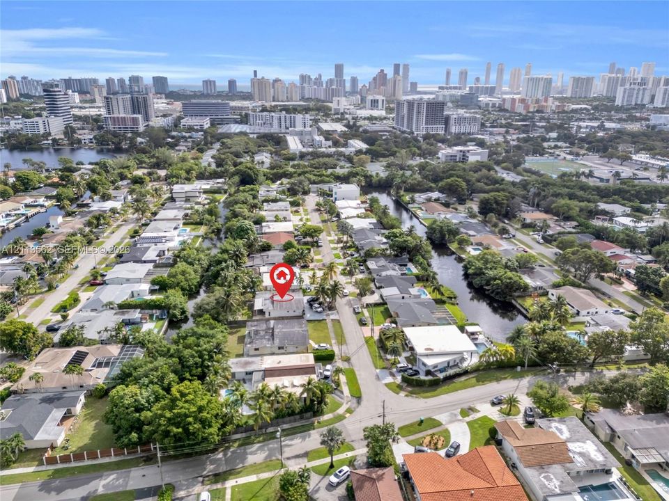 Aerial perspective featuring a canal-front property located within a dense residential area, inclusive of mature landscaping and a cityscape backdrop