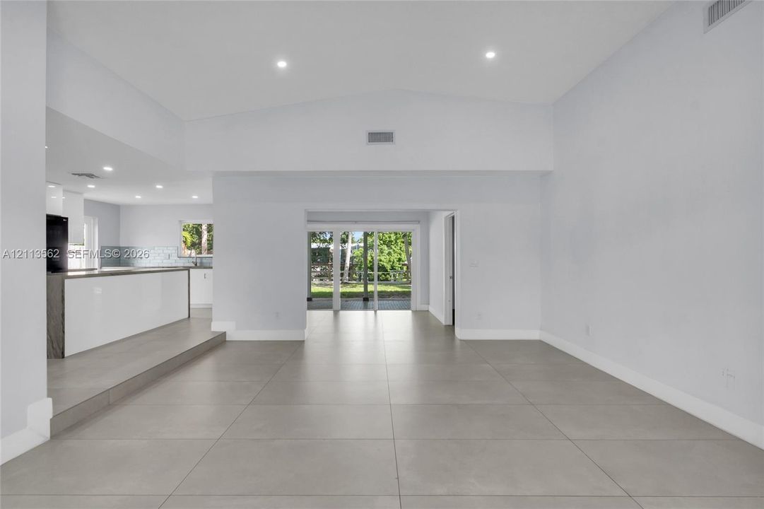 Open-concept interior featuring large-format tile flooring, vaulted ceilings, recessed lighting, and sliding glass doors
