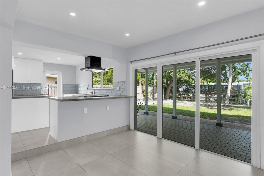 Kitchen featuring white cabinetry, a stone-surface breakfast bar, a modern range hood, and tile backsplash, with large sliding glass doors leading to a paved patio