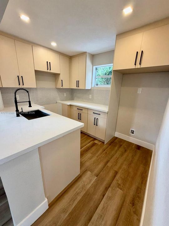 Kitchen featuring light-toned cabinetry, solid-surface countertops, wood-finish flooring, a hexagonal-pattern backsplash, and a black gooseneck faucet with an undermount sink