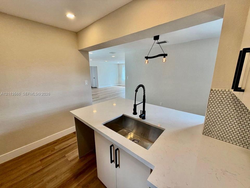 Kitchen area featuring quartz countertops, stainless steel undermount sink, matte black gooseneck faucet, custom cabinetry with matte black hardware, and wood-finish flooring