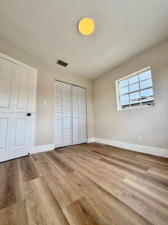 Interior space featuring wood-finish flooring, white louvered-style bi-fold closet doors, a multi-pane window, and a white paneled door