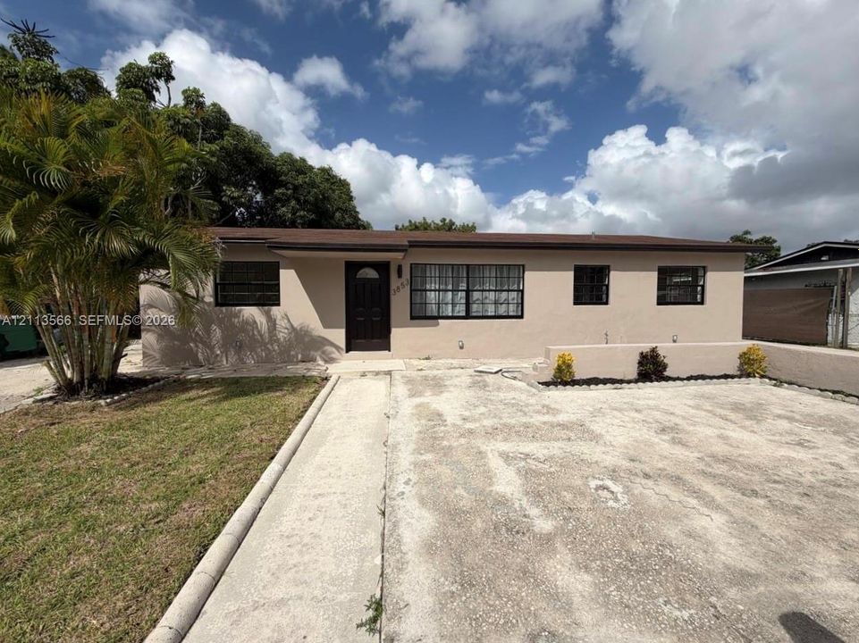 Single-story residence featuring a stucco exterior, concrete driveway, front entrance with arched glass panel, and mature landscaping