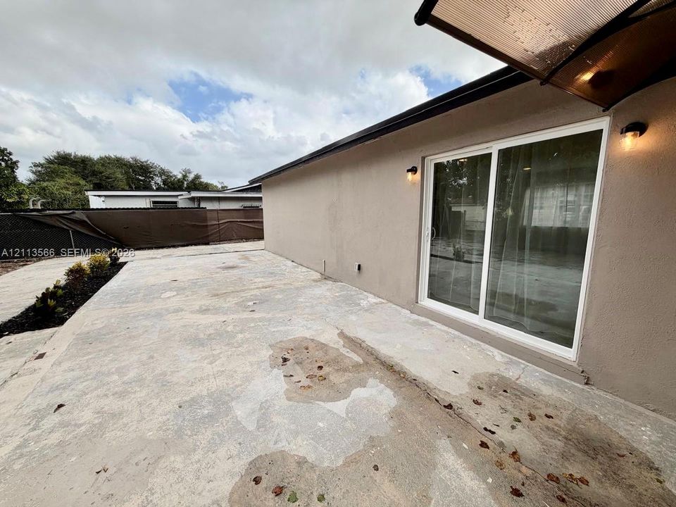 Concrete patio area featuring sliding glass doors, exterior wall-mounted lighting, and a dark-toned privacy fence