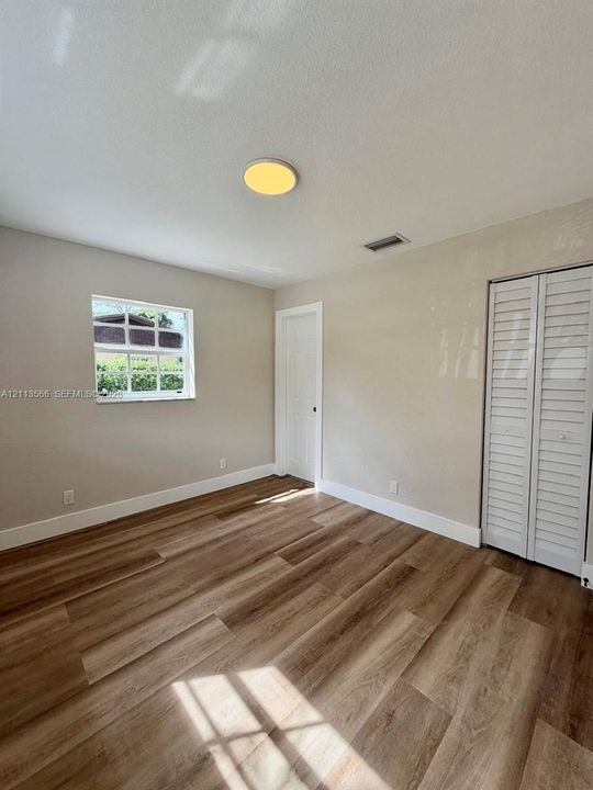 Room interior featuring wood-finish flooring, a single-hung window, white louvered closet doors, a neutral paint palette, and a flush-mount ceiling light fixture
