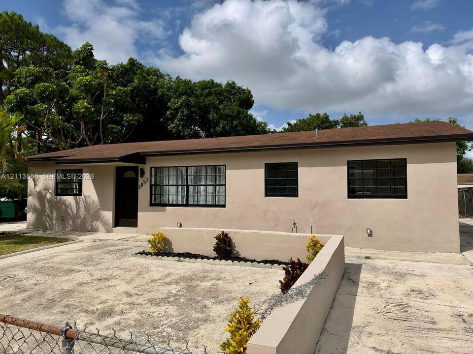 Single-story residence featuring a smooth stucco exterior, asphalt shingle roof, dark-framed grid windows, and a low-profile concrete retaining wall