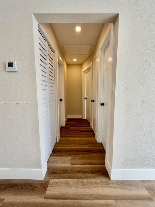 Hallway featuring wood-finish flooring, white paneled doors with black hardware, white louvered closet doors, and recessed ceiling lighting