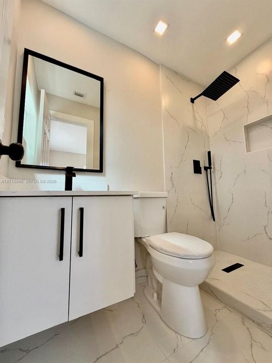 Bathroom featuring a white cabinet vanity with a matte black faucet, wall-mounted mirror with a black frame, walk-in shower with integrated niche and matte black rainfall showerhead, and large-format tile flooring