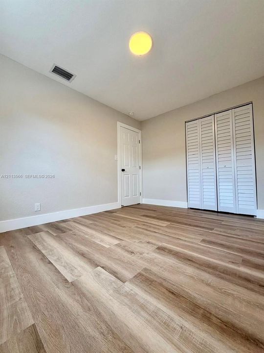 Wood-finish flooring, neutral wall tones, white six-panel interior door, and dual-panel white louvered closet doors