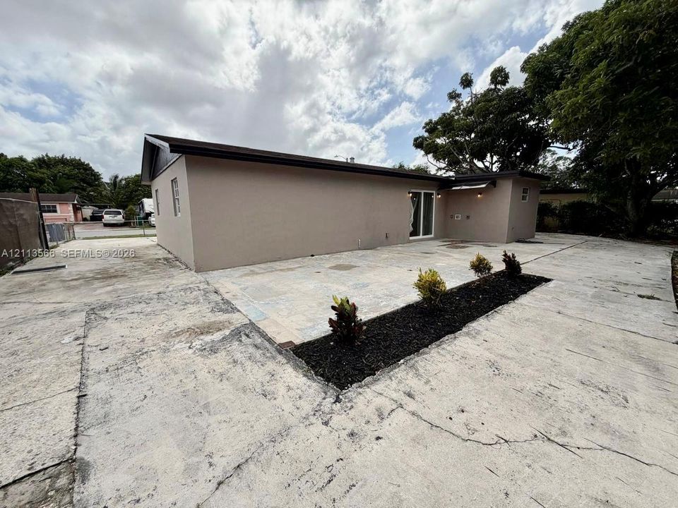 Stucco exterior siding, paved concrete driveway, integrated stone-paver patio area, and a dedicated landscape bed with shrubbery
