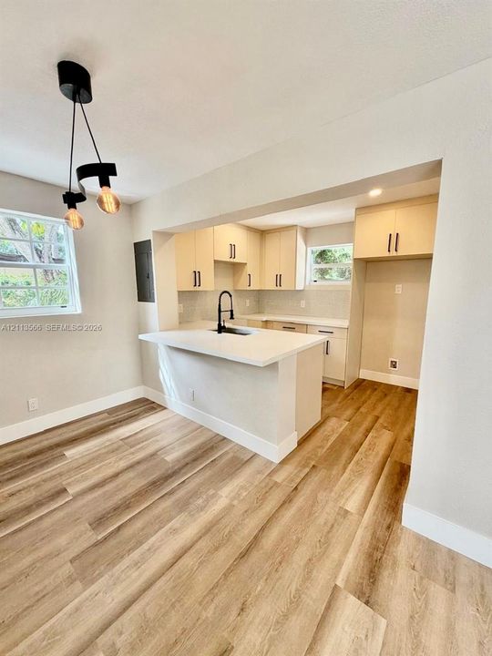 Kitchen featuring wood-finish flooring, quartz countertops, matte black plumbing fixtures, cabinetry with dark hardware, and a contemporary pendant light fixture
