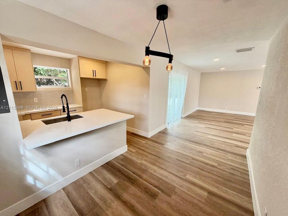 Kitchen featuring quartz countertops, wood-finish flooring, a matte black faucet, hexagonal backsplash tile, and an industrial-style pendant light fixture