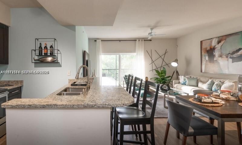 Kitchen featuring a breakfast bar, stone-finish countertops, stainless steel dual-basin sink, and dark cabinetry, with wood-finish flooring throughout