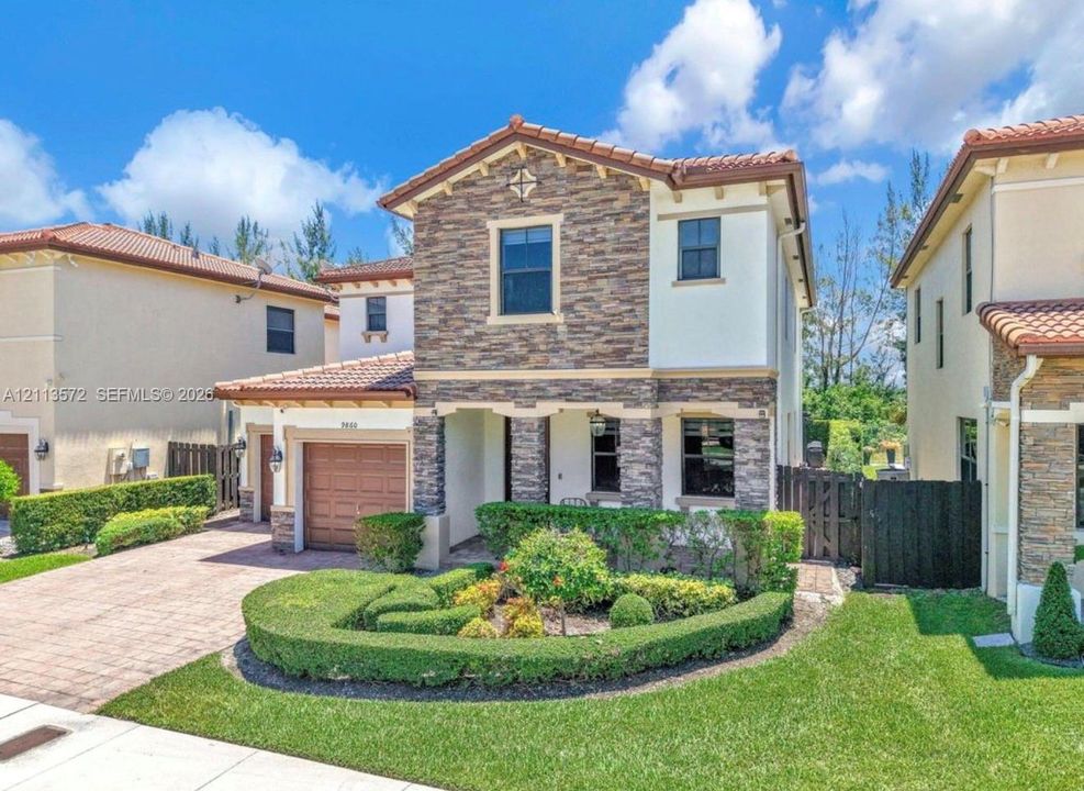 Two-story residence featuring a tile roof, decorative stone veneer façade, manicured landscaping, and a paved driveway