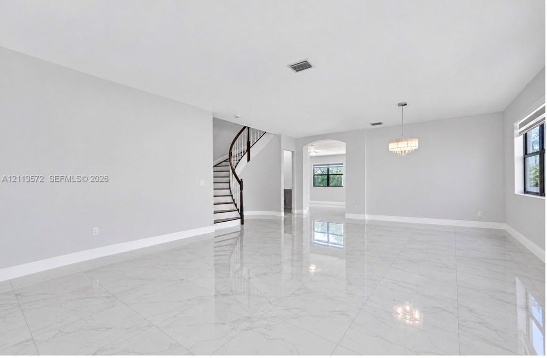Open-concept interior featuring large-format polished stone-finish flooring, a curved staircase with a dark wood handrail, an arched entryway, and a tiered drum chandelier