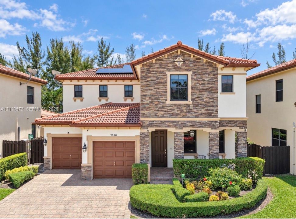 Stucco and multi-textured stone exterior featuring a tile roof, solar panels, paver driveway, and professional landscaping