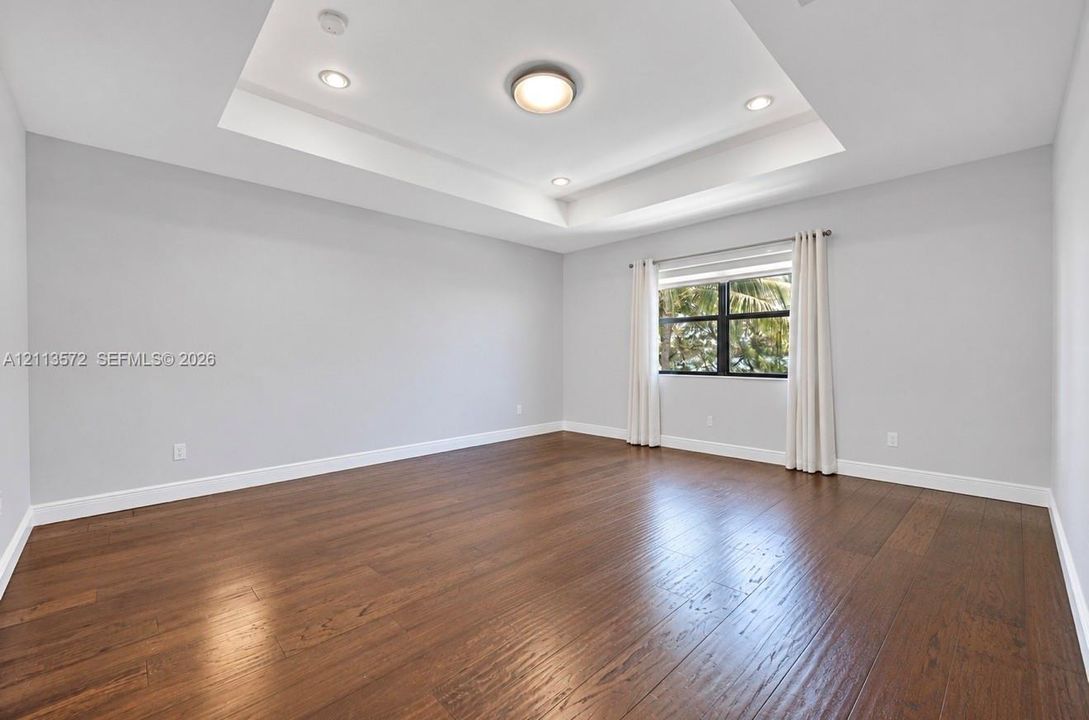 Tray ceiling with recessed lighting, wood-finish flooring, and a single-pane window with a dark frame
