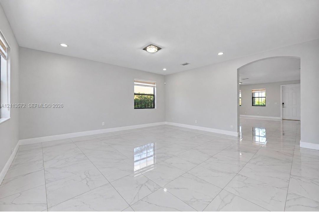 Large-format tile flooring, recessed lighting, archway architectural detailing, and neutral wall tones