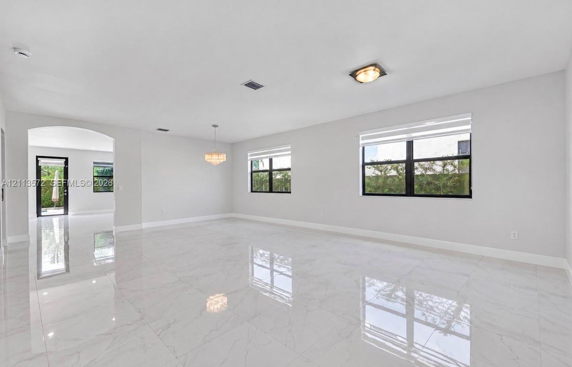 Open-concept interior featuring large-format polished tile flooring, black-framed windows, a multi-light chandelier, and an arched entryway