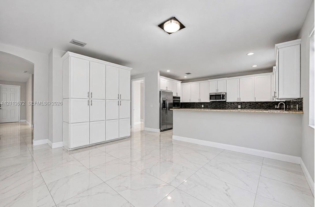 Kitchen featuring white shaker-style cabinetry, a stone-patterned breakfast bar, stainless steel appliances, and large-format porcelain tile flooring