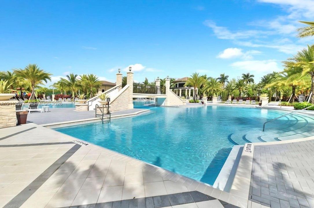 Expansive swimming pool featuring a decorative pedestrian bridge, stone-finish columns, tiered entry steps, and paved surround