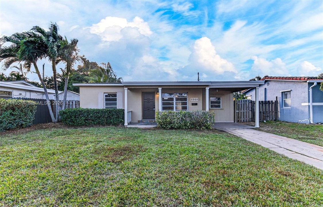Single-story exterior featuring a stucco facade, covered carport, concrete driveway, and front lawn landscaping