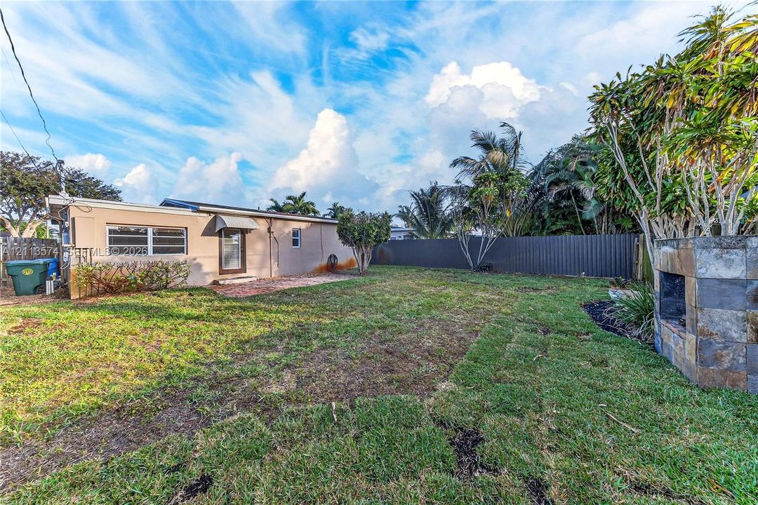 Backyard featuring a stone-clad outdoor fireplace, grass lawn, and perimeter fencing