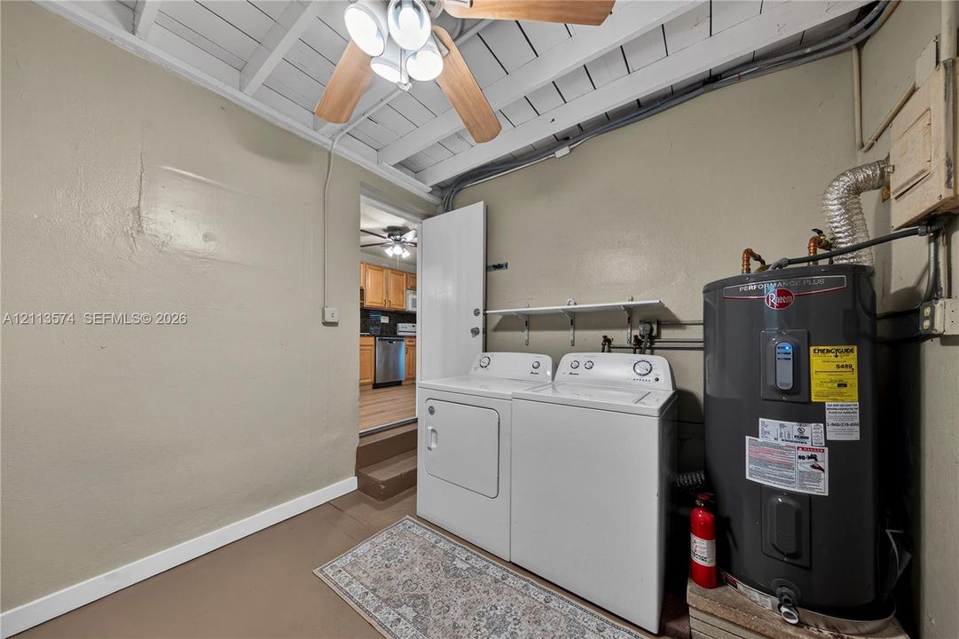 Utility area featuring an exposed beam ceiling, wall-mounted shelving, and a dedicated tank-style water heater