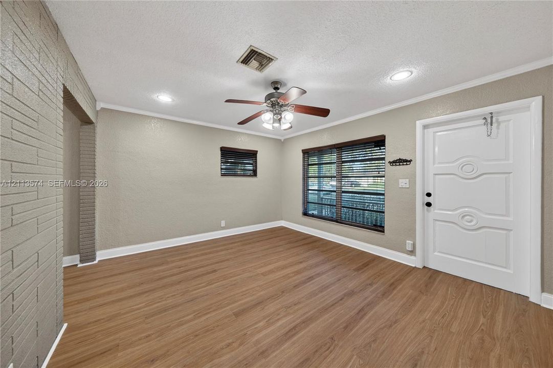 Interior space featuring wood-finish flooring, a textured brick accent wall, a central ceiling fan with integrated lighting, recessed lighting, and a white paneled entry door