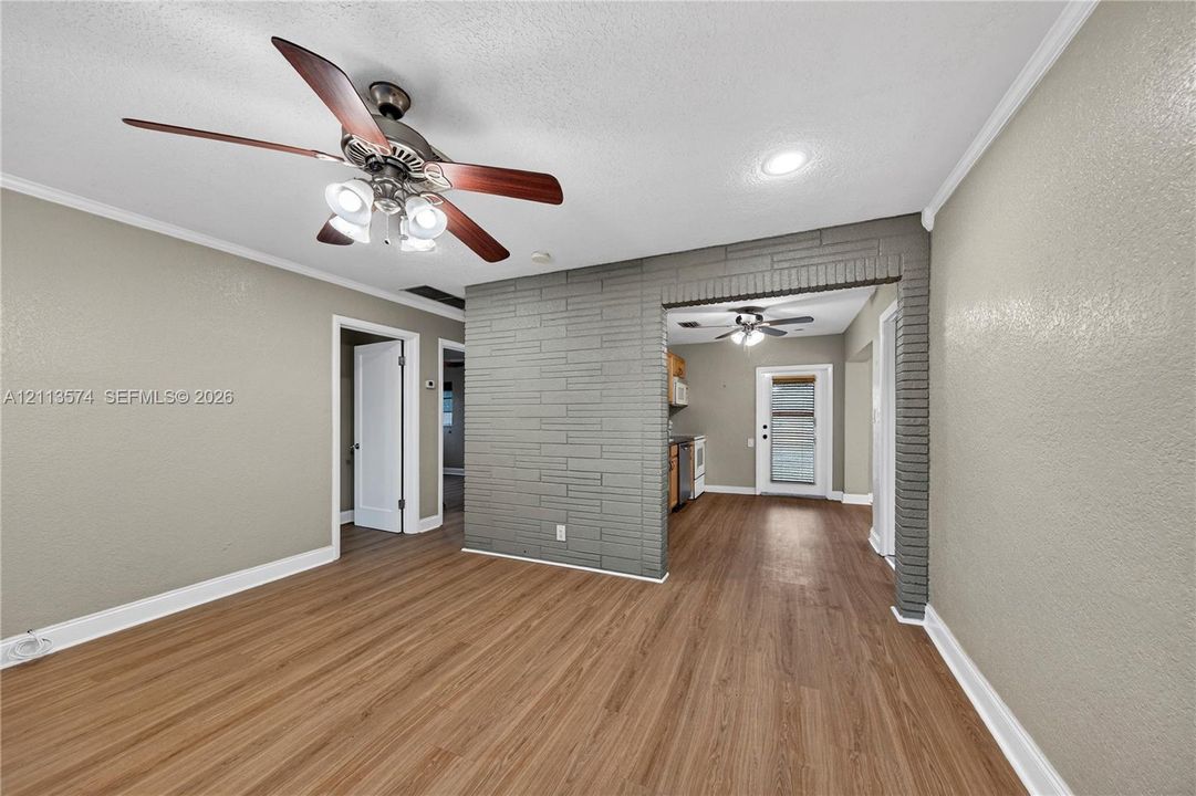 Living area featuring wood-finish flooring, a neutral color palette, grey painted brick accent wall, and ceiling fan with multi-light fixture