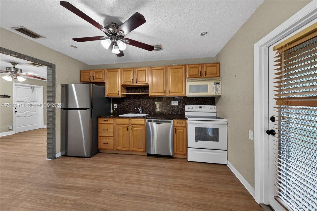 Kitchen featuring wood cabinetry, stone-finish countertops, stainless steel appliances, wood-finish flooring, and a ceiling fan with integrated lighting