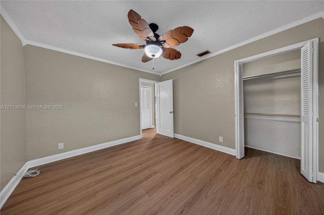 Wood-finish flooring, ceiling fan with stylized leaf-shaped blades, and closet with white louvered bifold doors
