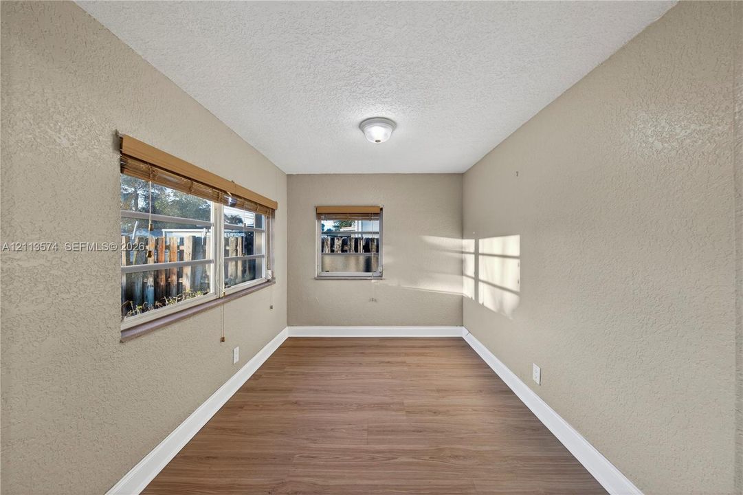Neutral-toned interior room featuring wood-finish flooring, dual windows with integrated blinds, and a centered flush-mount ceiling light fixture