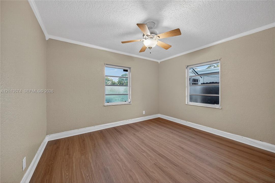 Room featuring wood-finish flooring, textured walls, dual windows, and a ceiling fan with integrated lighting