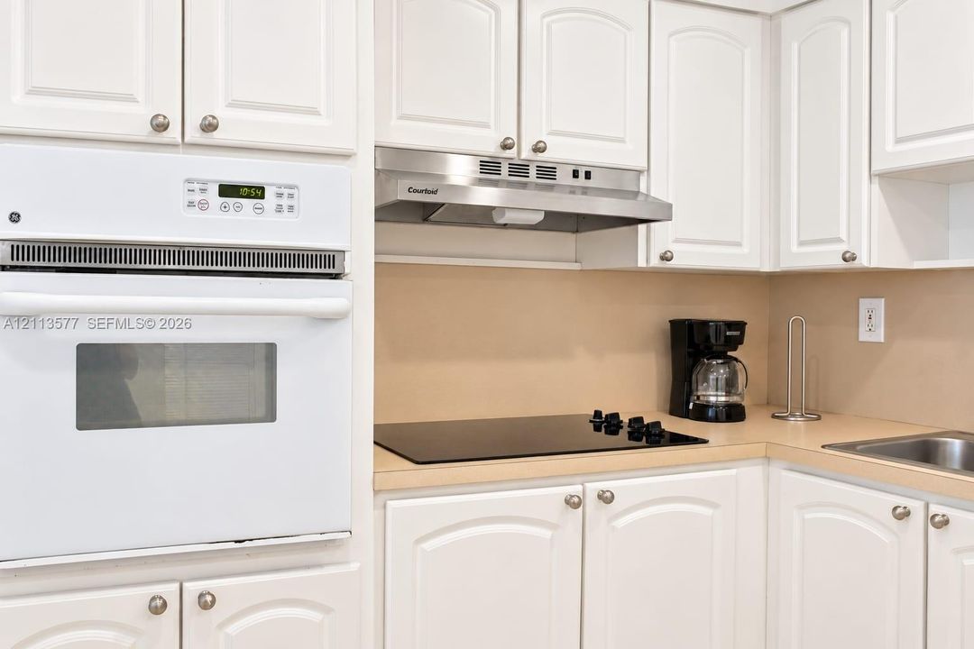 Kitchen featuring white raised-panel cabinetry, built-in white wall oven, stainless steel range hood, smooth-top electric cooktop, and solid-surface countertops