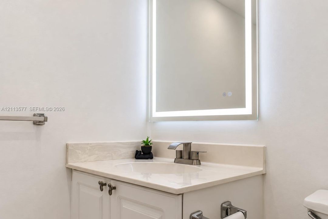 Built-in vanity with integrated countertop and sink, brushed metallic faucet, and wall-mounted illuminated mirror