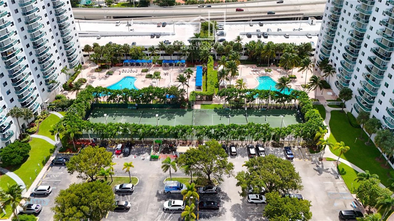 High-rise community featuring dual outdoor swimming pools, multi-court tennis facilities, paved parking, and landscaped grounds